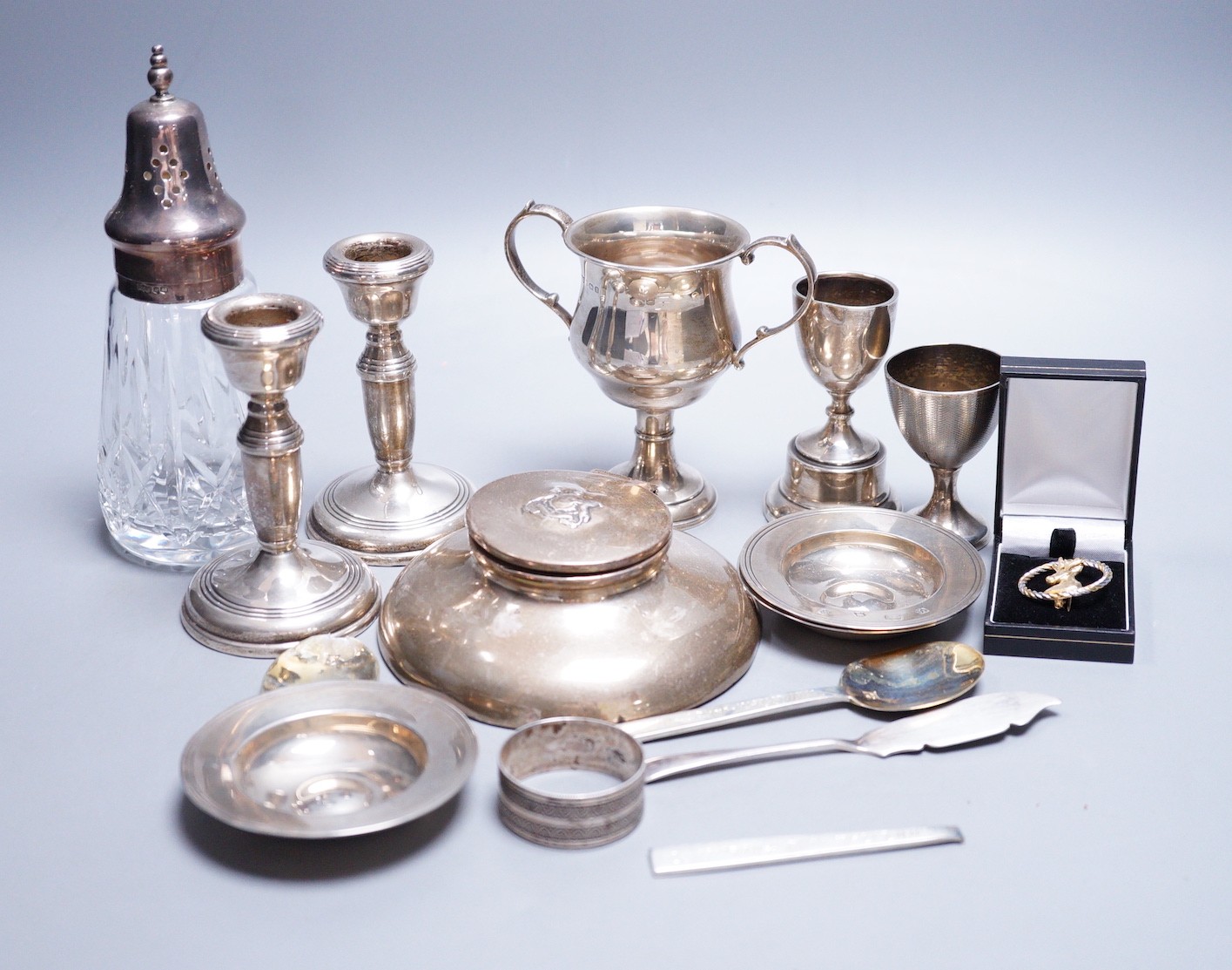 A small collection of assorted small silver, including a capstan inkwell, pair of dwarf candlesticks, two small trophy cups, egg cup, flatware, napkin ring, glass caster, a modern parcel gilt silver stag brooch and three